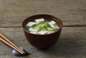 Japanese Miso Soup with Spring Onion and Cubed Tofu Cheese, In a Brown Bowl, Wooden Table photo