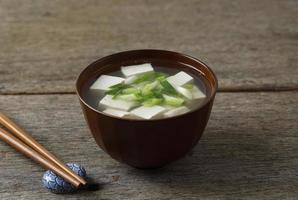 sopa de miso japonesa con cebolleta y queso de tofu en cubos, en un tazón marrón, mesa de madera foto