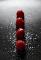 Red raspberries in a row with sugar on top on a black griddle. Backlighting. Vertical image. photo