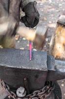 smith forges steel bar to produce nail on anvil photo