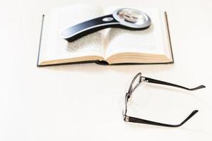 spectacles and magnifying glass on open book photo