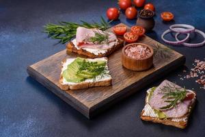 Sándwiches frescos y deliciosos de jamón, mantequilla, aguacate y semillas de sésamo en una tabla de cortar de madera foto
