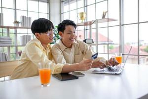 las parejas gays asiáticas usan una computadora portátil o compran en línea con tarjeta de crédito, concepto lgbtq. foto