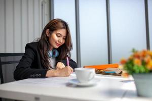 Portrait of Asian beautiful business woman working at the office, writing a document on table. photo