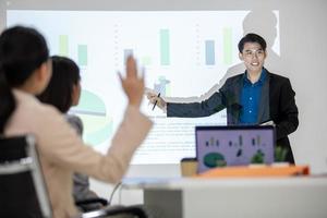 los colegas masculinos y femeninos del equipo de negocios asiático que hablan en el trabajo comparten ideas con el gráfico a bordo, los colegas levantaron la mano para hacer preguntas. foto