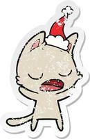 talking cat distressed sticker cartoon of a wearing santa hat vector