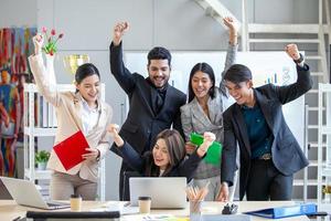 Asian business team celebrate corporate victory together in office, laughing and rejoicing, smiling excited employees colleagues screaming with joy in office. photo