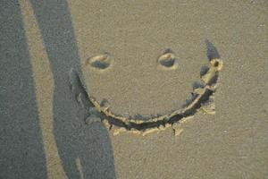 A smiley face drawing on a sand. With someone shadow. photo