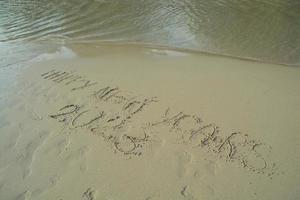 feliz año nuevo 2023 escrito a mano en la arena frente al mar. foto