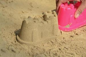 castillo de arena en la playa con juguetes de plástico rosa para niños. foto