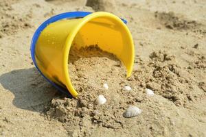 Juguete de cubo amarillo para niños con arena y juego de conchas en la playa. vacaciones con niños en el mar. foto