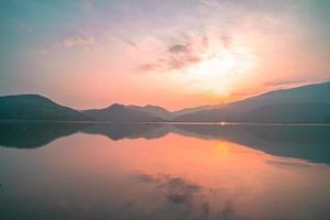 Panorama scenic of mountain lake with perfect reflection at sunrise. beautiful mountain range landscape with pink pastel sky with hills on background and reflected in water. Nature lake landscape