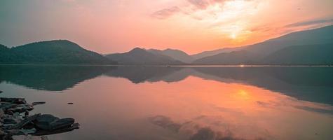 panorama escénico del lago de montaña con reflejo perfecto al amanecer. hermoso paisaje montañoso con cielo rosa pastel con colinas en el fondo y reflejado en el agua. naturaleza lago paisaje foto