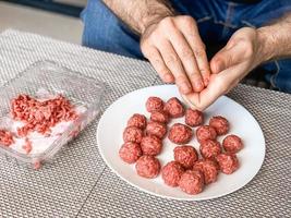 manos de hombre preparando albóndigas con carne picada cruda foto