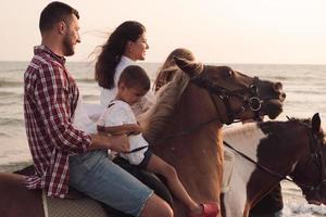 The family spends time with their children while riding horses together on a beautiful sandy beach on sunet. photo