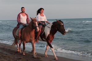 a loving young couple in summer clothes riding a horse on a sandy beach at sunset. Sea and sunset in the background. Selective focus photo