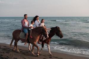 The family spends time with their children while riding horses together on a beautiful sandy beach on sunet. photo