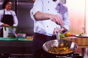 chef putting spices on vegetables in wok photo