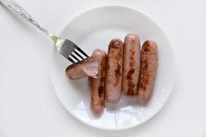 Fried meat sausages on a white plate with a fork. Delicious breakfast of sausages. photo