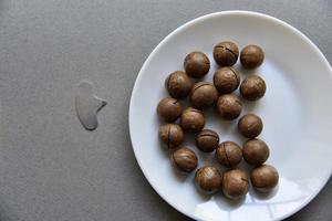 Macadamia nut in a dish with a bottle opener on a gray background. Macadamia nut prepared for use in a vase. Delicious breakfast of nuts. photo