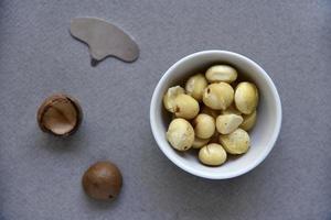 Delicious peeled Macadamia nut in a salad bowl on a gray background. The kernels of a delicious Macadamia nut close-up. photo