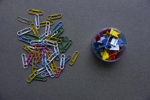 clips de papel multicolores sobre un fondo gris y en un frasco. clips de papel sobre un fondo gris. foto