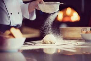 chef sprinkling flour over fresh pizza dough photo