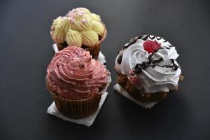 Sweet cakes with cream and sprinkles on a black background. Delicious pies for breakfast on black. photo