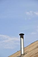Metal chimney on the roof of an old house. Chimney chimney on the background of clouds of the sky. photo
