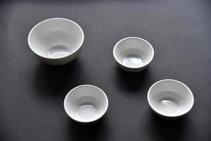 White porcelain salad bowls on a black background. Beautiful four white saucers on black. photo