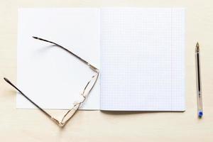 pen and eyeglasses on blank open school notebook photo