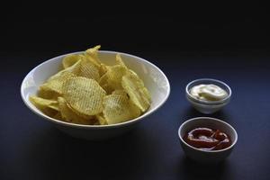 Delicious potato chips with sauces on a black background. Appetizer of potato chips with sauce. Fast food on a black background. photo