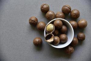 nuez de macadamia en un plato con un abrebotellas sobre un fondo gris. nuez de macadamia preparada para usar en un florero. delicioso desayuno de nueces. foto