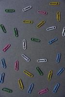 Multicolored iron paper clips on a gray background. Stationery paper fasteners scattered on a gray background like stars. photo