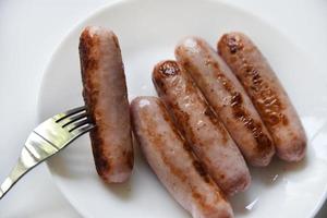 Fried meat sausages on a white plate with a fork. Delicious breakfast of sausages. photo