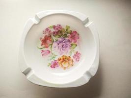 white cigarette ashtray with floral motif in the middle. ashtray isolated on a white background.  Ashtrays are often used by smokers to dispose of cigarette ashes or cigarette butts photo