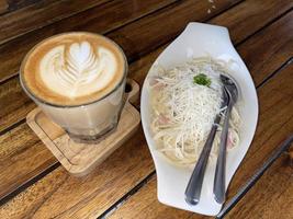 hermosa taza de café capuchino con arte latte y spaghetti alla carbonara foto