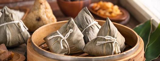 dumpling de arroz - comida china zongzi en un vapor sobre una mesa de madera con pared de ladrillo rojo, fondo de ventana en casa para el concepto del festival del bote del dragón, de cerca. foto