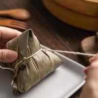 Comer zongzi - bola de arroz del festival del barco del dragón joven mujer asiática comiendo comida tradicional china en una mesa de madera en la celebración de la casa, cerrar foto