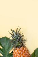 hermosa piña en hojas de monstera de palma tropical aisladas sobre fondo amarillo naranja pastel brillante, vista superior, puesta plana, sobre la fruta de verano. foto