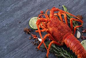 Cooked boiled lobster, delicious dinner seafood meal set with knife and fork on black stone slate background, restaurant menu design, close up, overhead photo