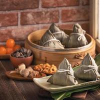 dumpling de arroz - comida china zongzi en un vapor sobre una mesa de madera con pared de ladrillo rojo, fondo de ventana en casa para el concepto del festival del bote del dragón, de cerca. foto