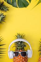 Funny pineapple wearing white headphone, listen music, isolated on yellow background with tropical palm leaves, top view, flat lay design concept. photo