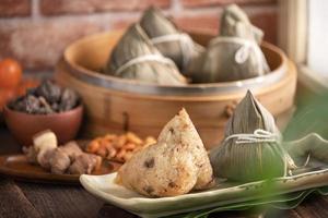 zongzi - bola de masa hervida de arroz chino zongzi en un vapor sobre una mesa de madera con ladrillo rojo, fondo de ventana en casa para el concepto del festival del bote del dragón, de cerca. foto