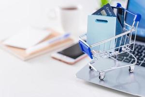 Office online paying, stay home shopping, electronic payment with credit card concept, laptop on white table background with shop cart, close up. photo