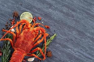 Cooked boiled lobster, delicious dinner seafood meal set with knife and fork on black stone slate background, restaurant menu design, top view, overhead photo