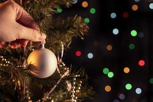 Christmas background concept- beautiful decor bauble hanging on the Christmas tree with sparkling light spot, blurry dark black background, copy space, close up. photo