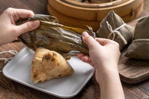 Comer zongzi - bola de arroz del festival del barco del dragón joven mujer asiática comiendo comida tradicional china en una mesa de madera en la celebración de la casa, cerrar foto