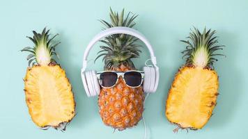 piña divertida con auriculares blancos, concepto de escuchar música, aislada en un fondo de color con hojas de palma tropical, vista superior, diseño plano. foto