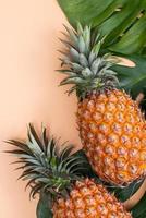 Beautiful pineapple on tropical palm monstera leaves isolated on bright pastel orange yellow background, top view, flat lay, overhead above summer fruit. photo